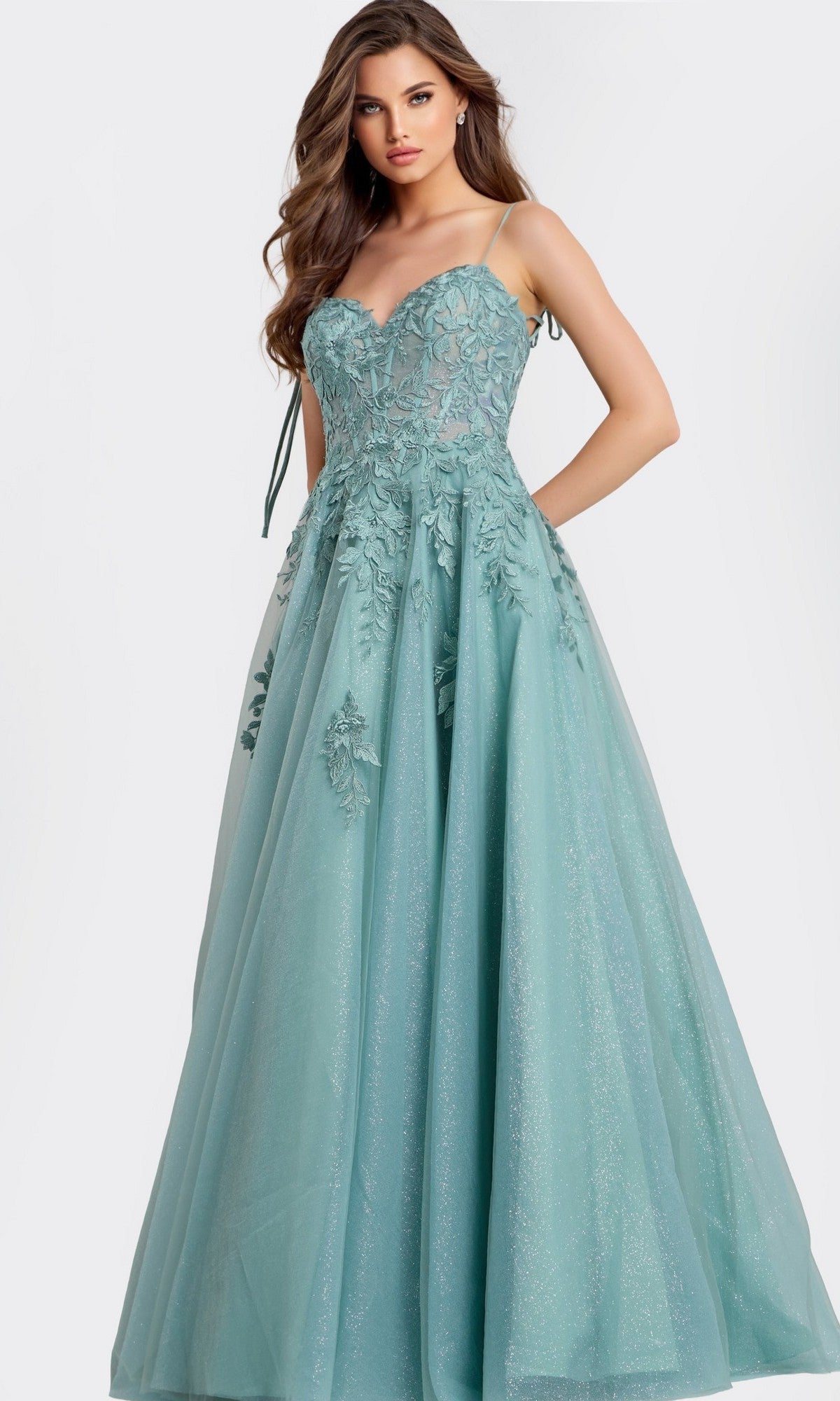 A woman wearing the Jovani 49092 long prom dress in sage, featuring a sleeveless design with delicate floral lace appliques on the bodice and a voluminous floor-length skirt.